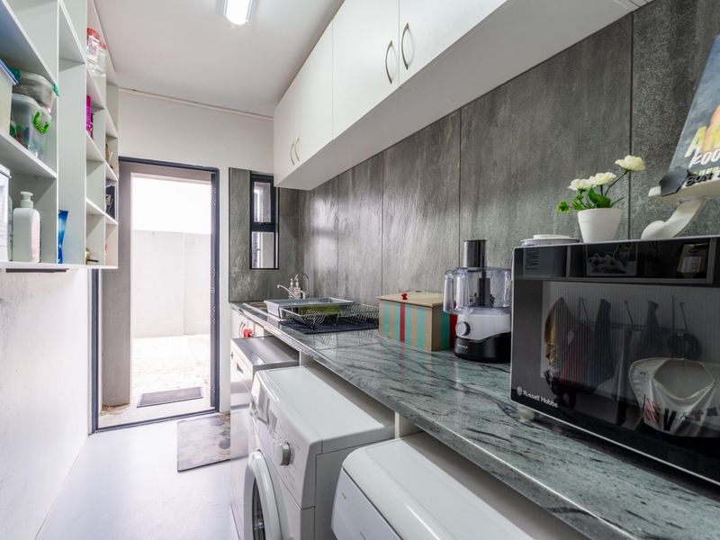 A functional scullery featuring stone countertops, built-in cabinetry, open shelving, and a stainless steel sink with direct access to an outdoor area.