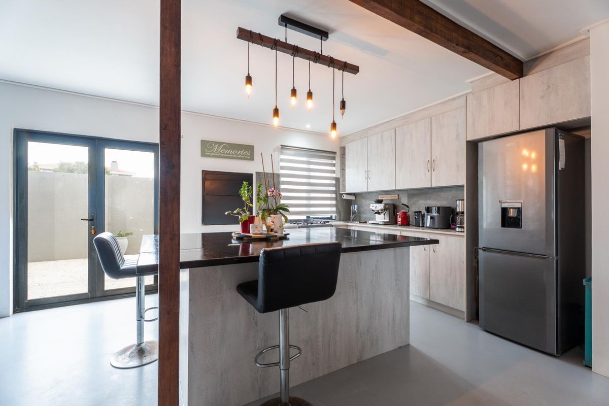 Modern kitchen featuring a central island with breakfast bar, light wood-grain cabinetry, exposed timber beam, and direct access to an outdoor patio area.