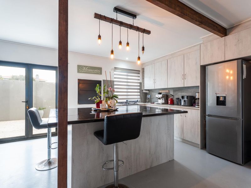 Modern kitchen featuring a central island with breakfast bar, light wood-grain cabinetry, exposed timber beam, and direct access to an outdoor patio area.