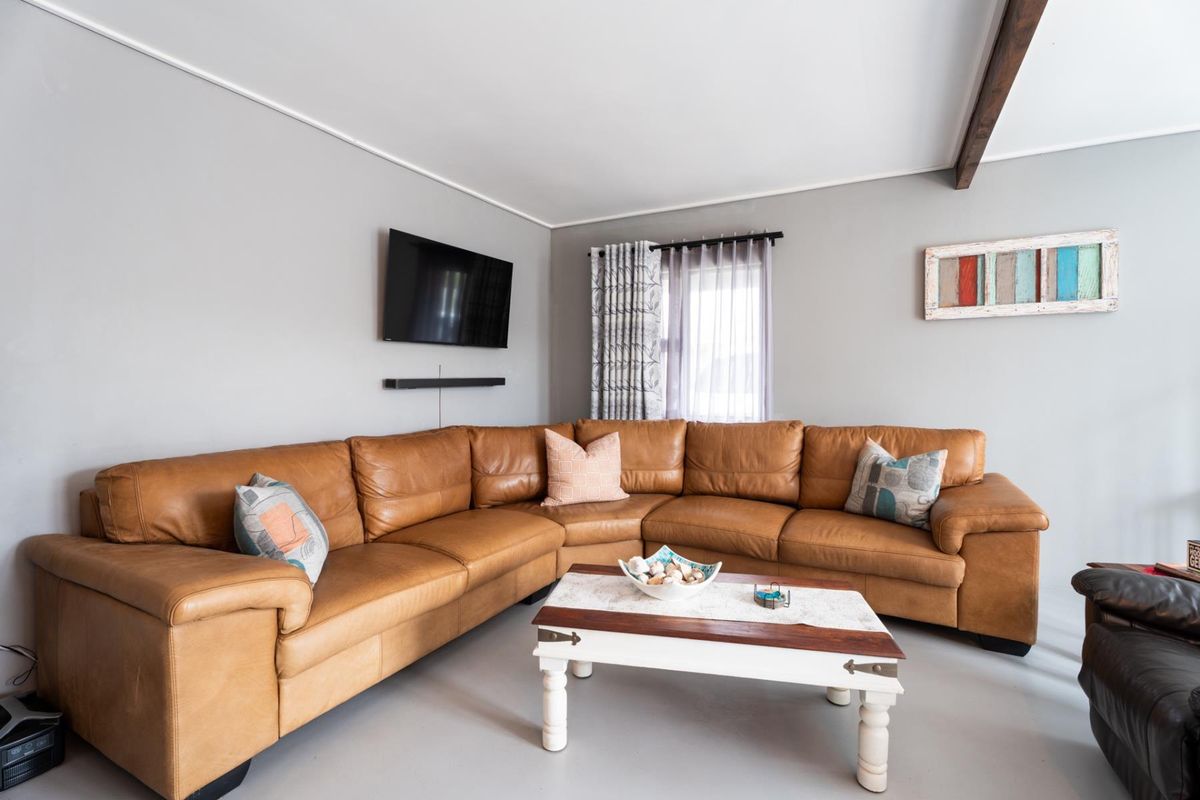 A comfortable living room featuring neutral wall tones, an exposed ceiling beam, and natural light through a window with fitted curtain hardware.