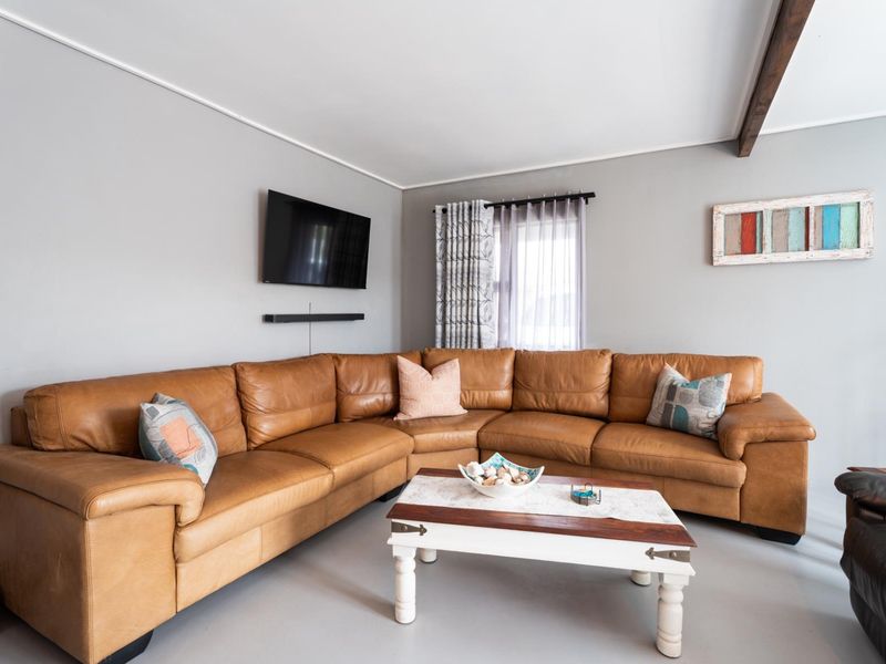 A comfortable living room featuring neutral wall tones, an exposed ceiling beam, and natural light through a window with fitted curtain hardware.