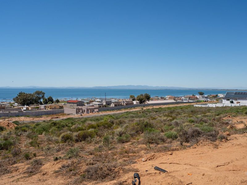 An elevated view of a vacant residential plot overlooking the coastline and ocean, showcasing the surrounding neighborhood and landscape.