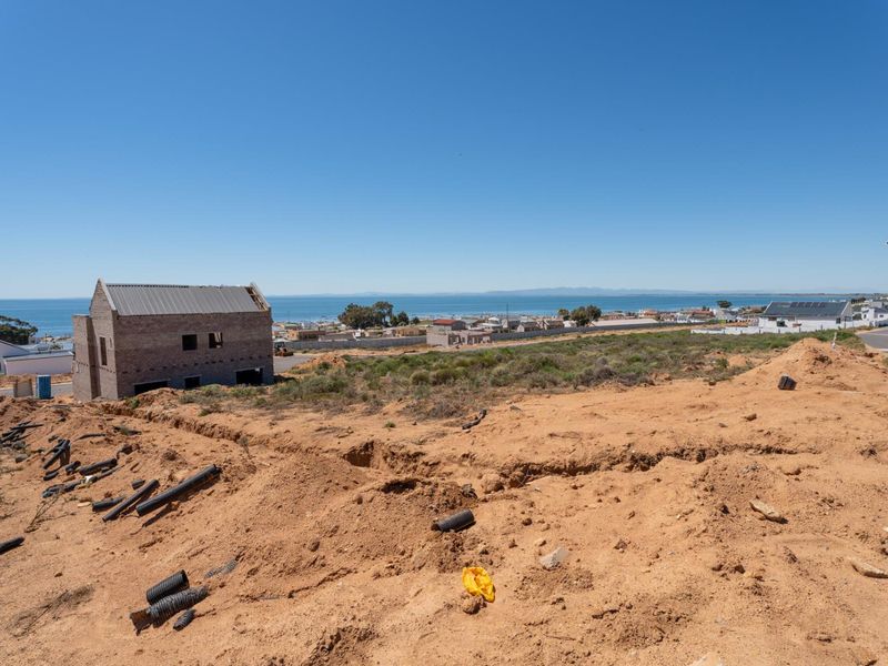 An elevated view of a vacant residential plot featuring coastal views and ongoing site preparation with nearby construction.