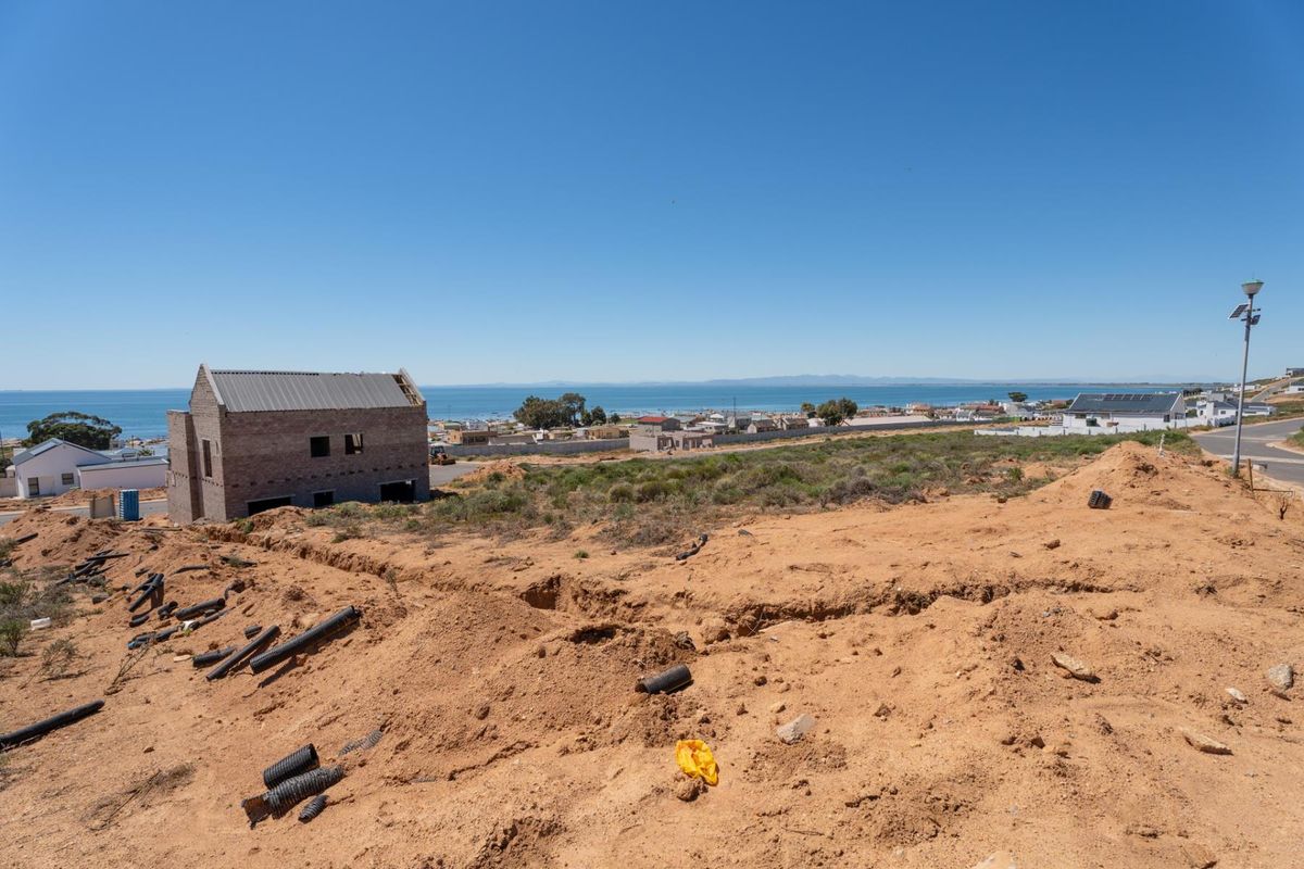 An elevated view of a vacant residential plot featuring coastal views and ongoing site preparation with nearby construction.