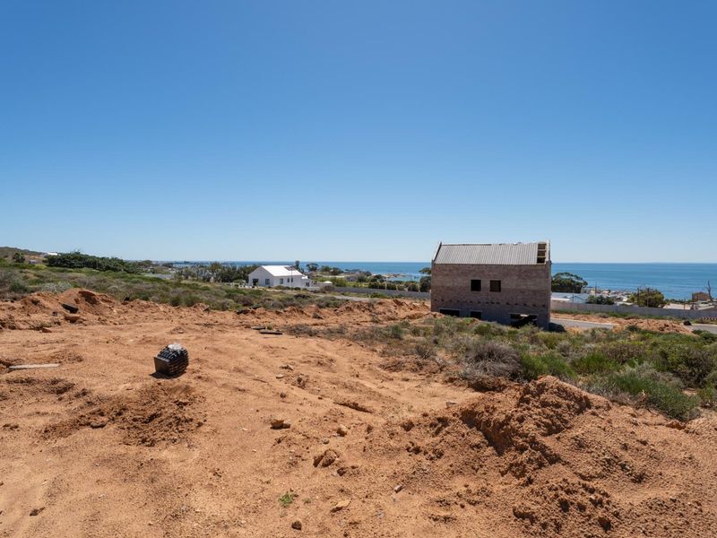 A vacant residential plot featuring an unfinished building structure with scenic coastal views and natural terrain.