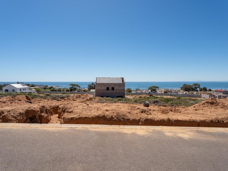 A vacant residential plot featuring uneven terrain and excavated soil, offering expansive coastal views in a developing neighborhood.