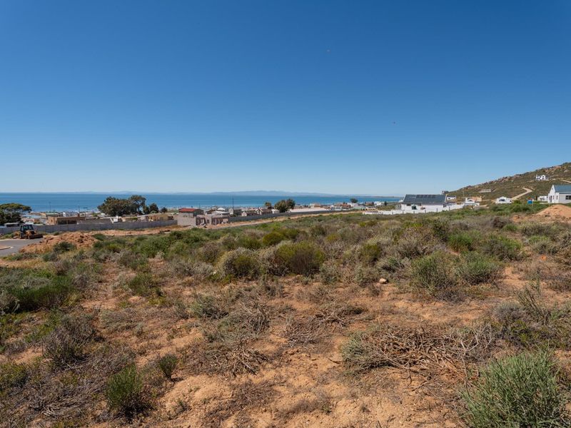 A wide-angle view of the vacant residential land featuring natural coastal vegetation and a clear outlook towards the ocean and surrounding neighborhood.