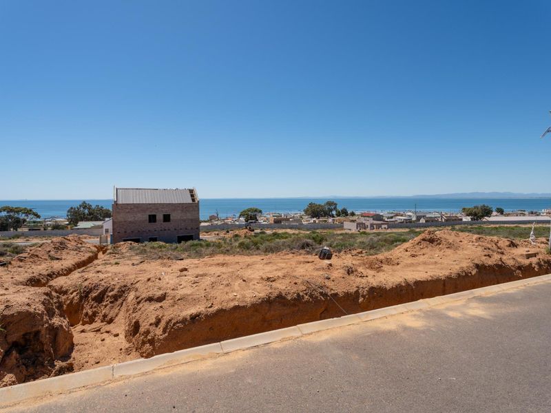A vacant residential plot featuring excavated ground, a street light, and distant ocean views, situated along a paved road.