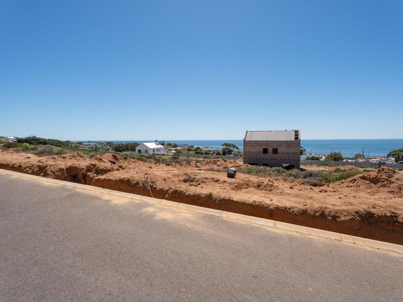 A street-level view of a vacant residential plot featuring paved road access and coastal views in the distance.