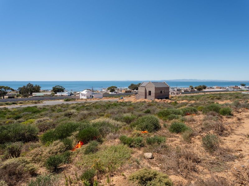 A wide-angle view of a coastal residential area featuring a vacant plot with native vegetation and distant ocean views.