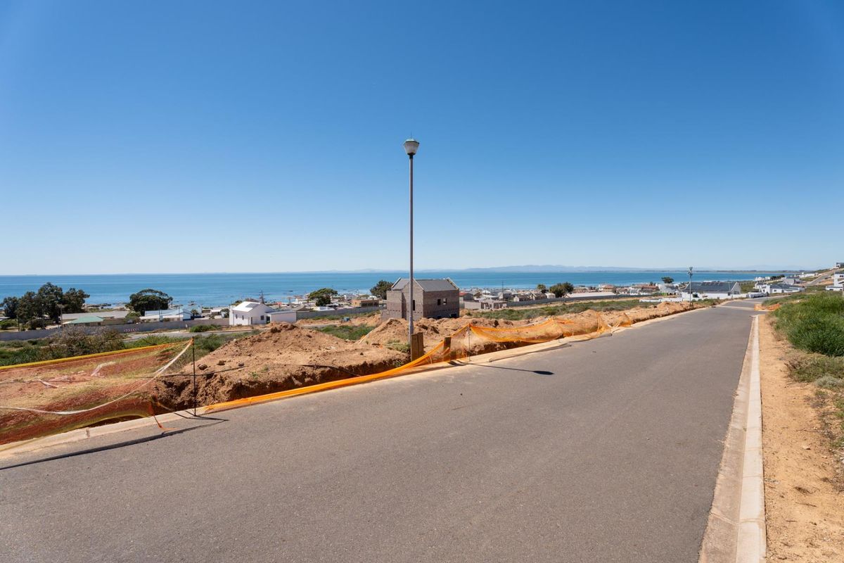A street-level view of a residential area featuring an asphalt road, street lighting, and distant coastal views.