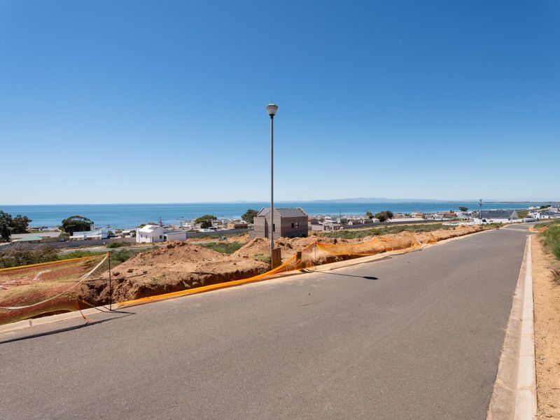 A street-level view of a residential area featuring an asphalt road, street lighting, and distant coastal views.