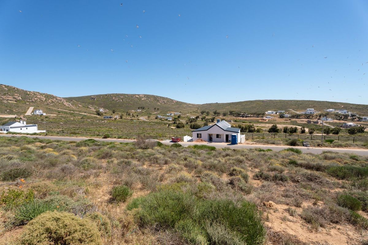 An elevated view of a residential plot featuring natural landscape, surrounding hills, and access to a paved road.