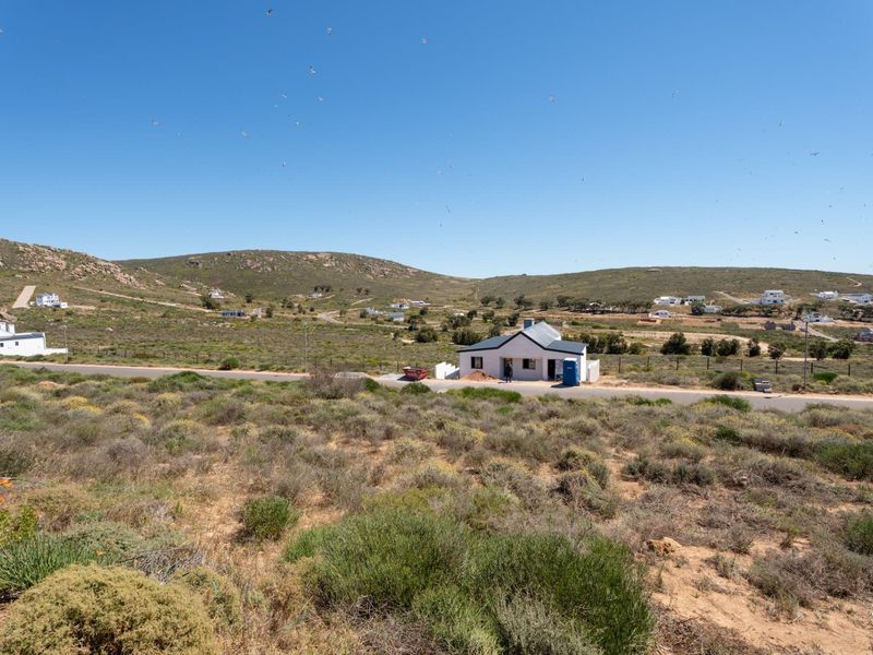 An elevated view of a residential plot featuring natural landscape, surrounding hills, and access to a paved road.