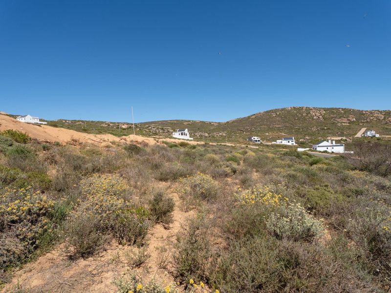A view of a vacant residential plot featuring natural coastal vegetation and surrounding hillside landscape.