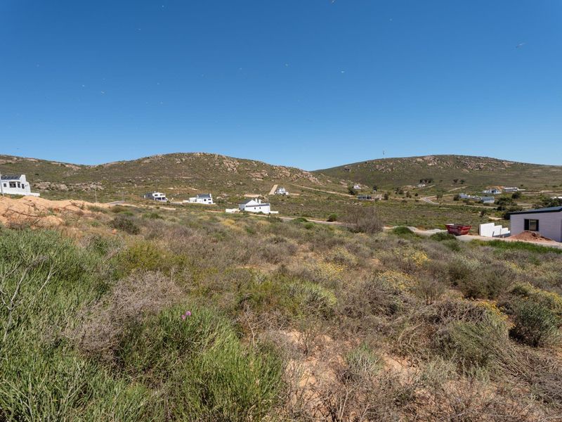 A wide-angle view of the vacant residential land, showcasing the natural landscape, surrounding hills, and nearby residential properties in the distance.