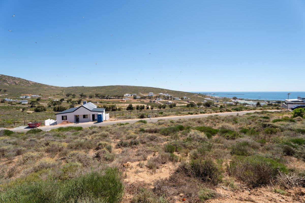 An elevated view of a vacant residential plot featuring coastal landscape, nearby road access, and surrounding neighborhood scenery.