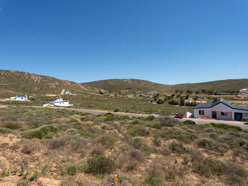 An elevated view of a residential development area featuring natural landscape, paved roads, and scattered coastal-style homes under a clear blue sky.