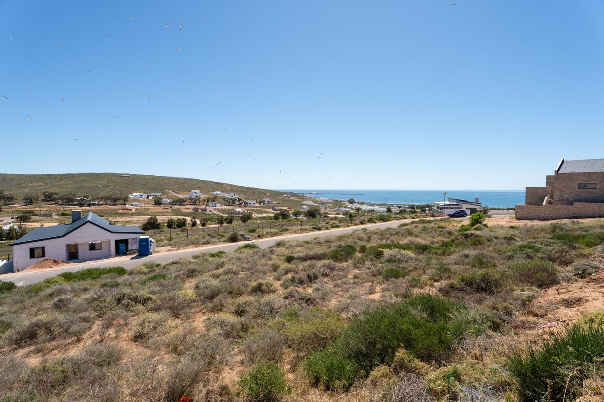 An elevated view of a vacant residential plot featuring natural coastal vegetation, surrounding neighborhood development, and a clear outlook towards the ocean.