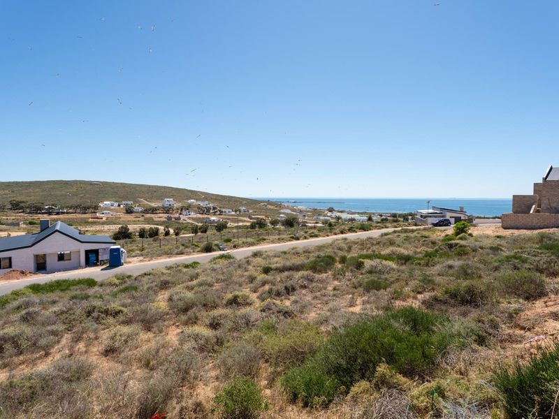 An elevated view of a vacant residential plot featuring natural coastal vegetation, surrounding neighborhood development, and a clear outlook towards the ocean.