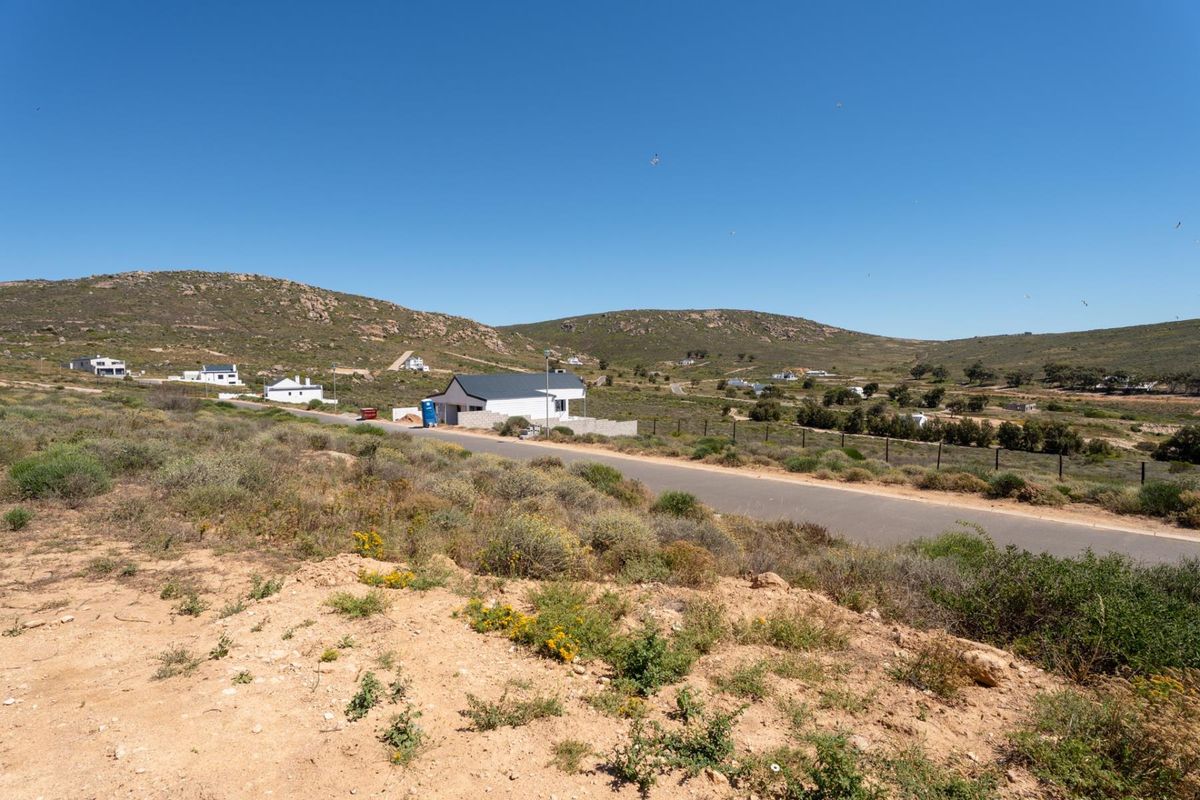 A wide-angle view of the vacant residential land, showcasing the surrounding hilly landscape, local road access, and nearby coastal residential development.
