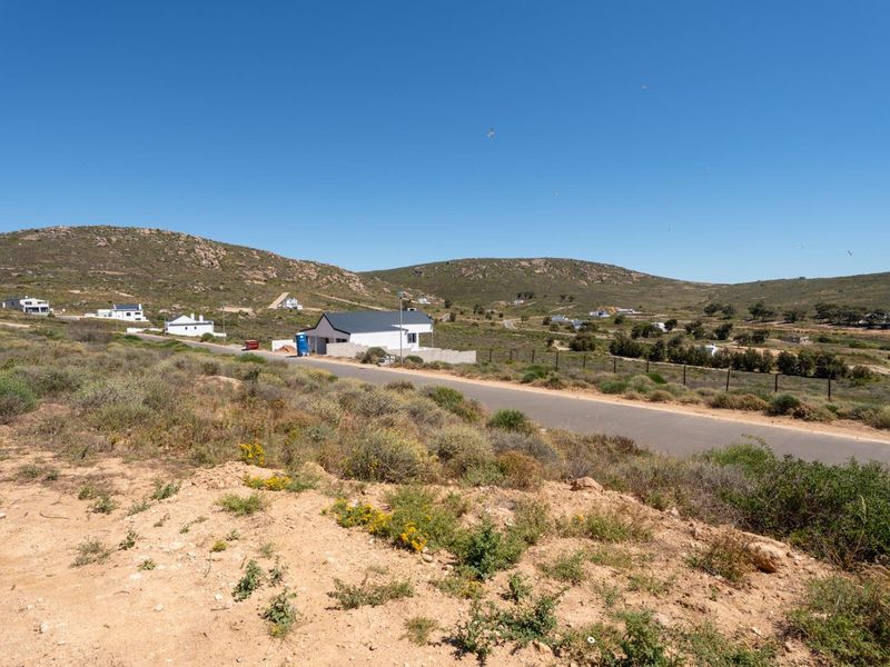 A wide-angle view of the vacant residential land, showcasing the surrounding hilly landscape, local road access, and nearby coastal residential development.