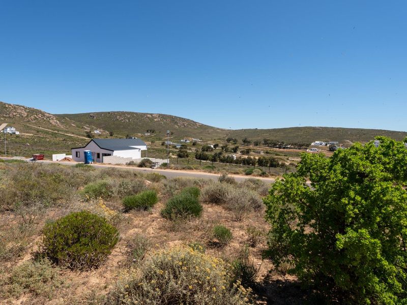 A wide-angle view of the vacant residential land, showcasing the surrounding natural landscape, local topography, and nearby road access.
