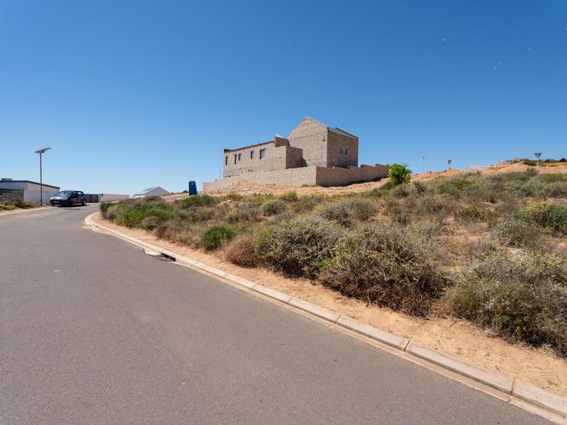 Street view of a residential plot featuring an unfinished masonry structure and natural vegetation in a developing neighborhood.