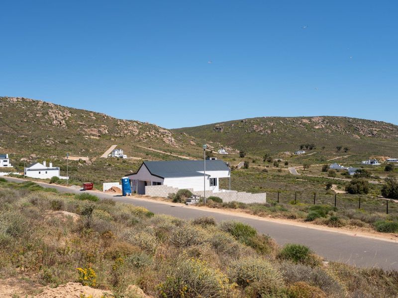 A view of a residential property under construction, featuring a metal roof and concrete block boundary walls, situated in a scenic hillside landscape.