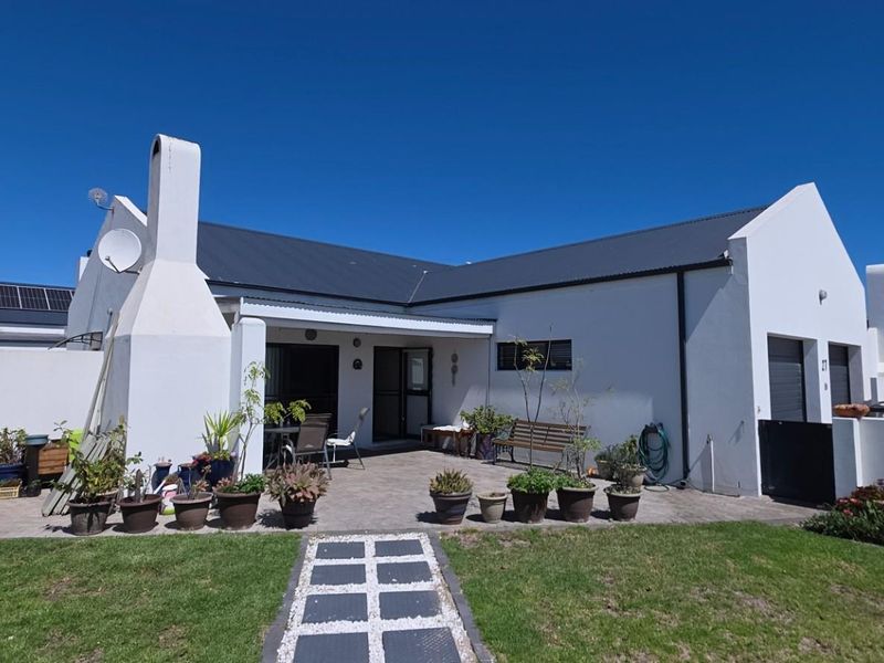 Rear view of the house featuring a paved patio area, an external fireplace chimney, and a well-maintained garden lawn.