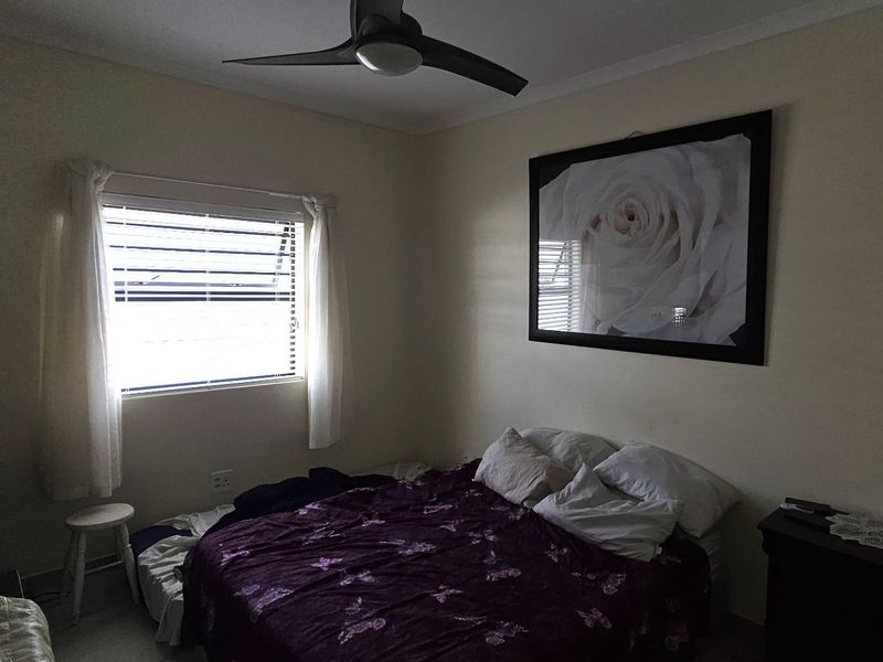 A standard bedroom featuring a ceiling fan and louver window, providing a functional space with neutral wall finishes.