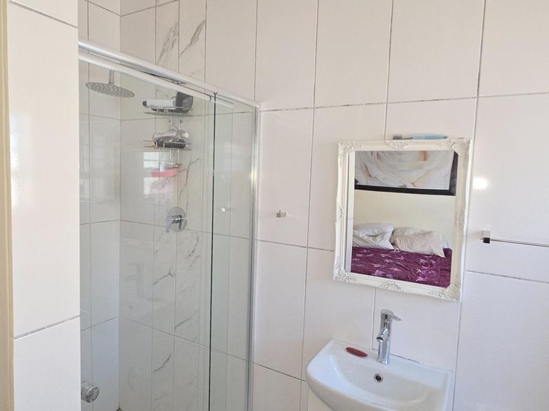 A clean, modern bathroom featuring a glass-enclosed shower with a rain shower head and a wall-mounted basin with a mixer tap.