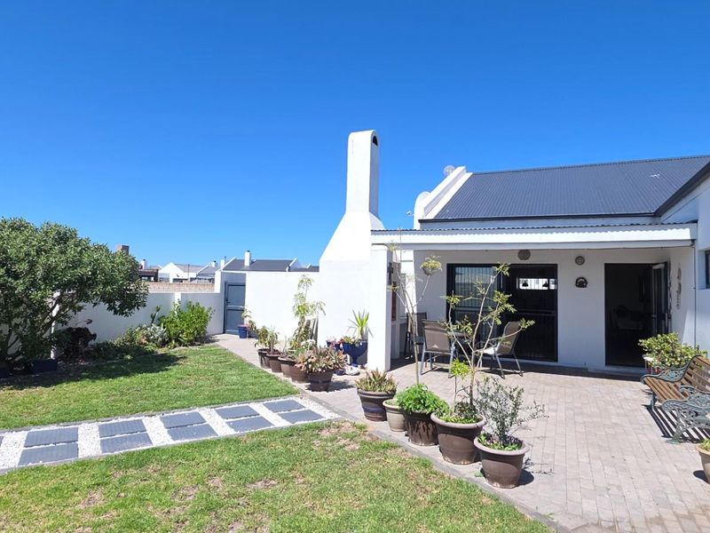 Rear view of the property featuring a paved patio area, an external fireplace chimney, and a landscaped garden with a stone pathway.