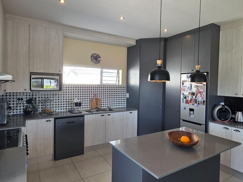 Modern kitchen featuring two-tone cabinetry, stone countertops, a central island, mosaic tile backsplash, and integrated appliances with contemporary pendant lighting.