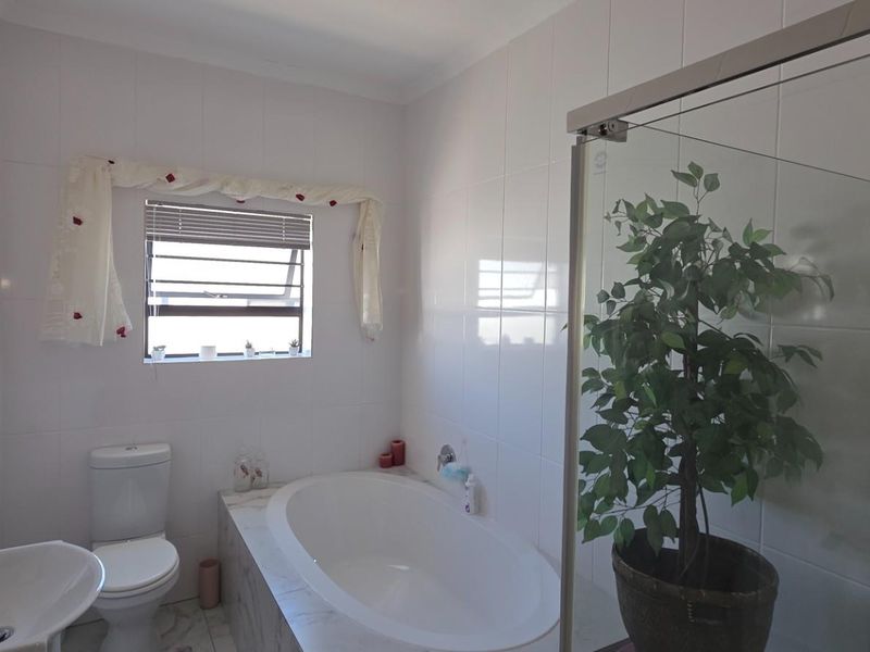 A clean, well-maintained bathroom featuring a built-in bathtub, a separate glass-enclosed shower, a pedestal washbasin, and a toilet with neutral wall tiling.