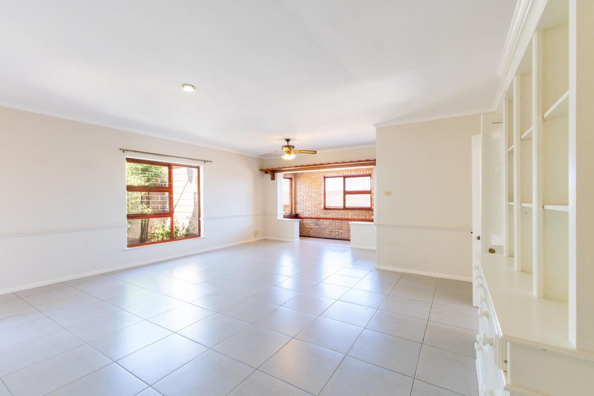 Spacious, light-filled living area featuring neutral tiled flooring, built-in cabinetry, and a charming exposed brick accent wall in the adjoining space.