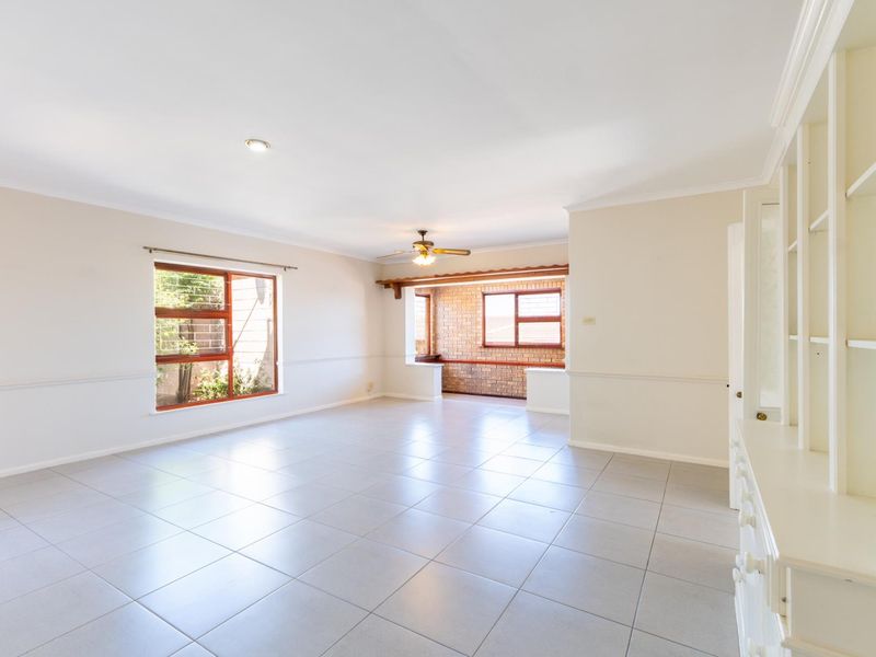 Spacious, light-filled living area featuring neutral tiled flooring, built-in cabinetry, and a charming exposed brick accent wall in the adjoining space.