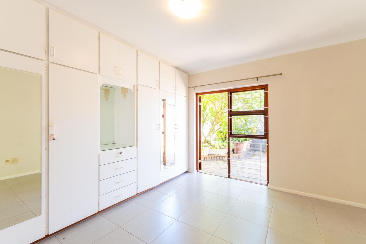 A bright, empty bedroom featuring extensive built-in cupboards, tiled flooring, and a sliding door providing direct access to the garden area.