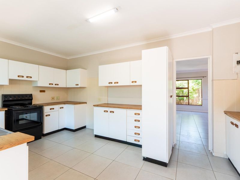 A functional kitchen featuring white built-in cabinetry, laminate countertops, a freestanding stove, and neutral ceramic floor tiles with a view into the adjacent living area.