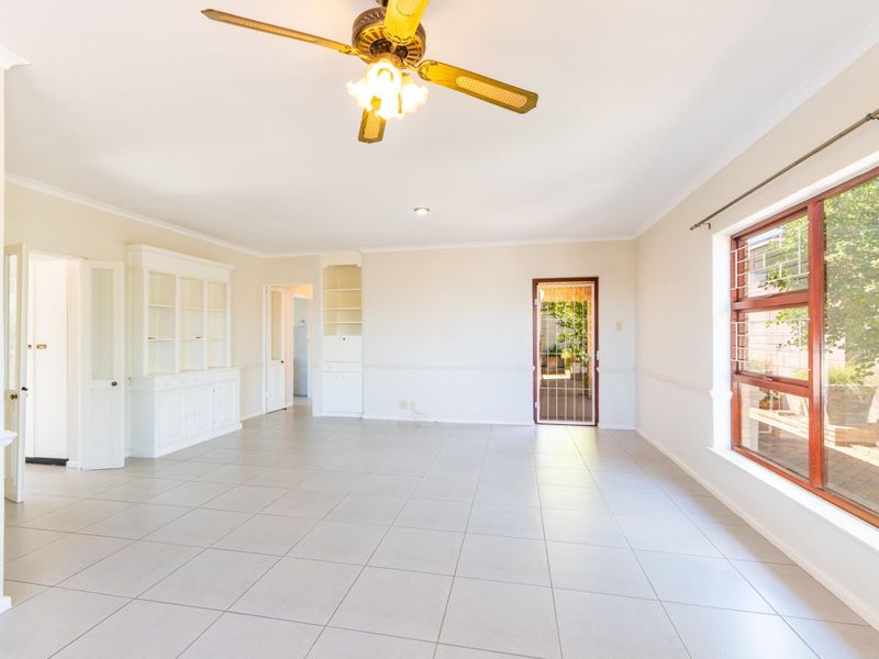 Spacious, light-filled living room featuring neutral tiled flooring, built-in display cabinetry, a ceiling fan, and direct access to an outdoor area.