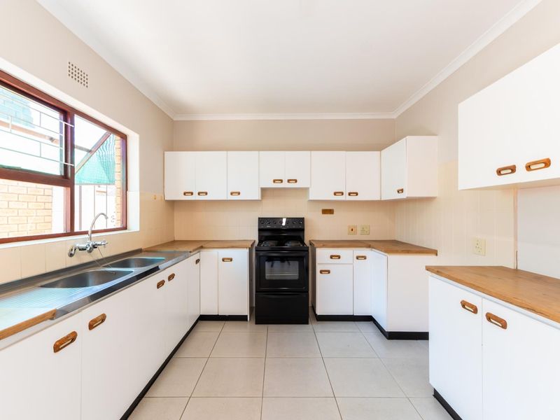 A clean, functional kitchen featuring white cabinetry, wooden countertops, tiled flooring, and a freestanding stove, offering a bright and practical workspace.