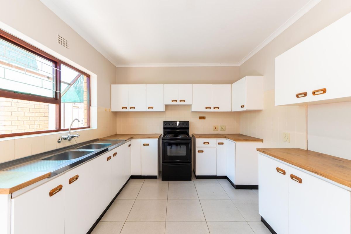 A clean, functional kitchen featuring white cabinetry, wooden countertops, tiled flooring, and a freestanding stove, offering a bright and practical workspace.