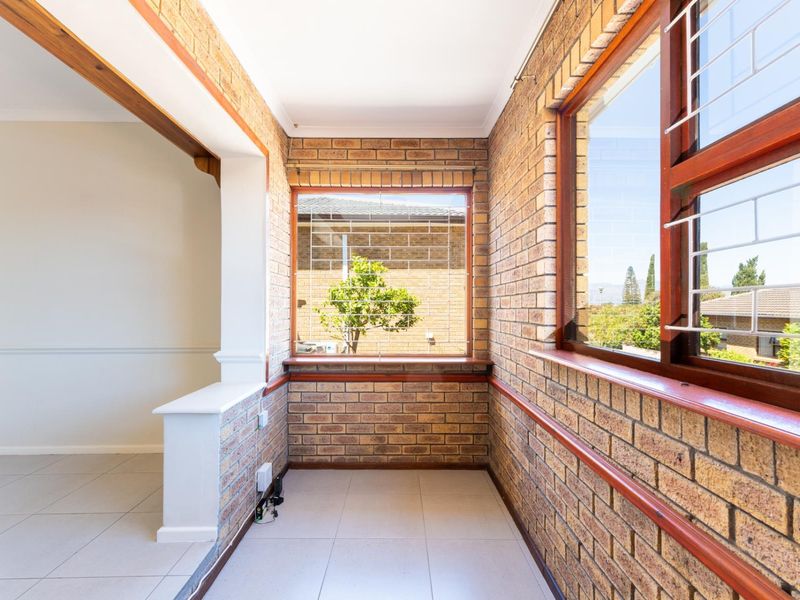 A bright, empty living area featuring exposed brick walls, tiled flooring, and large timber-framed windows with security bars.