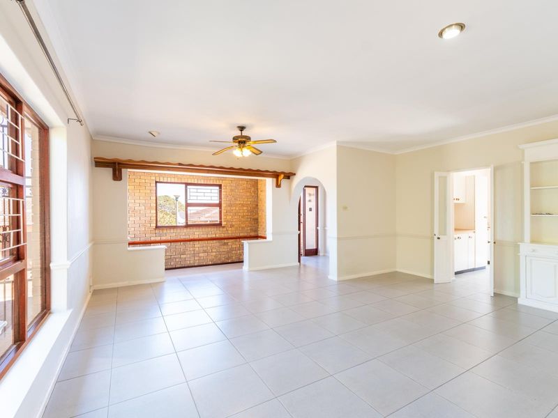 Spacious living area featuring tiled floors, an exposed brick feature wall, a ceiling fan, and a built-in display cabinet, offering a bright and open layout.