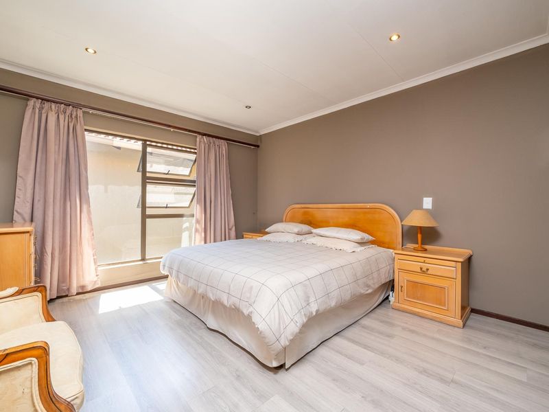 A well-lit bedroom featuring laminate flooring, recessed downlights, and neutral wall tones, providing a comfortable and functional sleeping space.