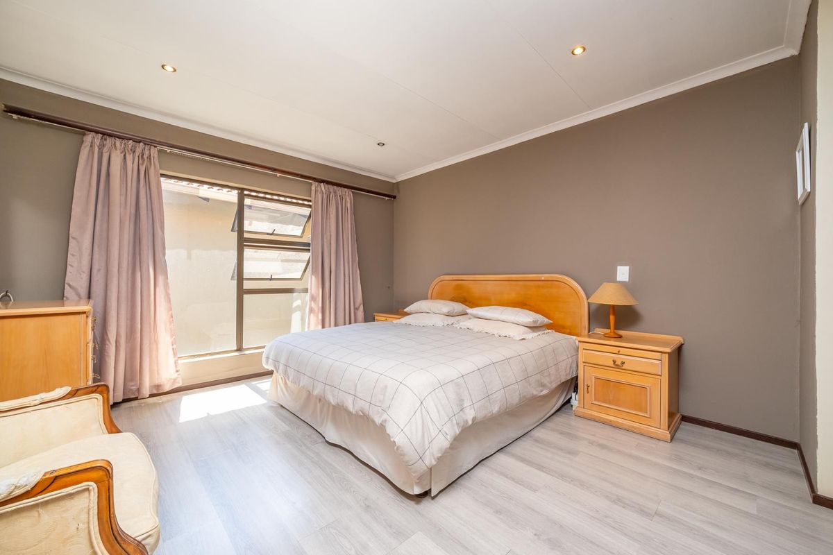 A well-lit bedroom featuring laminate flooring, recessed downlights, and neutral wall tones, providing a comfortable and functional sleeping space.