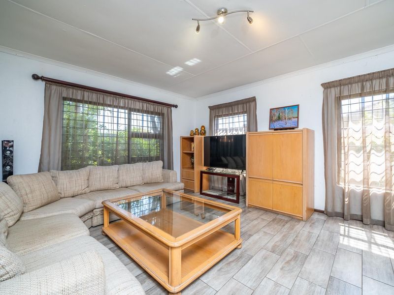 A comfortable living room featuring tiled flooring, large windows with security bars, and a central ceiling light fixture.