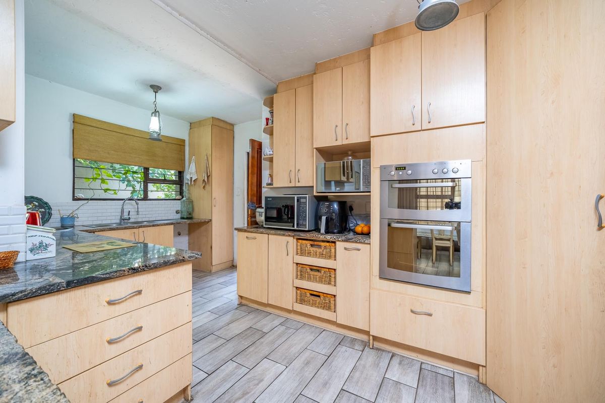 A functional kitchen featuring light wood cabinetry, granite countertops, a built-in double oven, and modern tiled flooring with ample storage space.