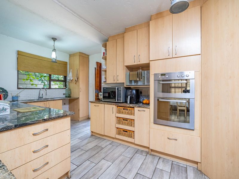 A functional kitchen featuring light wood cabinetry, granite countertops, a built-in double oven, and modern tiled flooring with ample storage space.