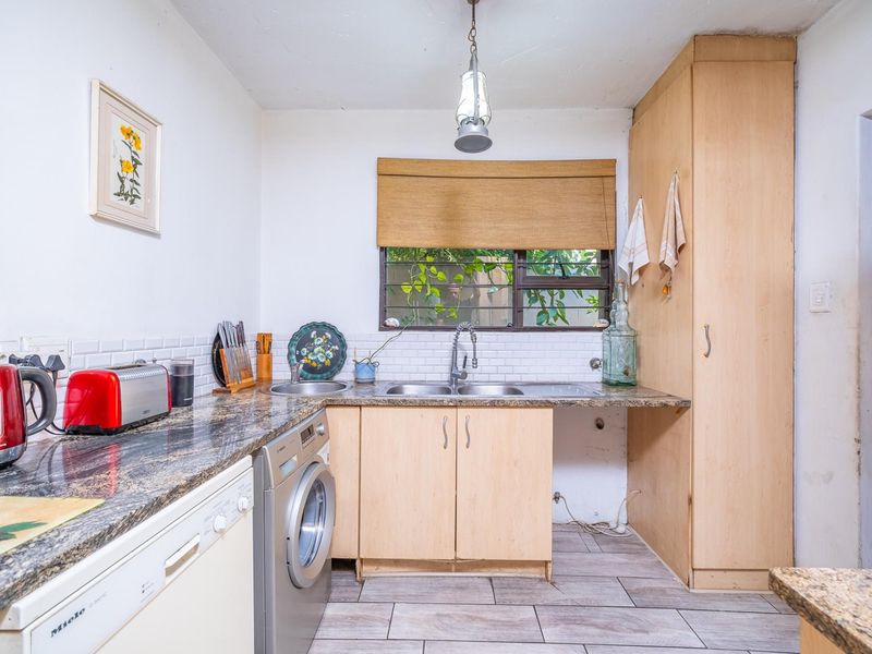 Functional kitchen featuring granite countertops, subway tile backsplash, double basin sink, and ample built-in cabinetry with space for laundry appliances.